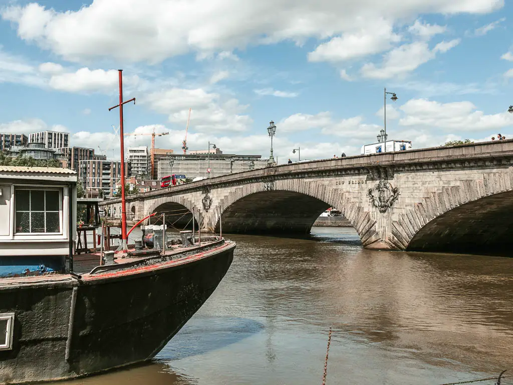 Looking over the river to the stone archway kew bridge. There is the front of a boat poking into the frame on the left.