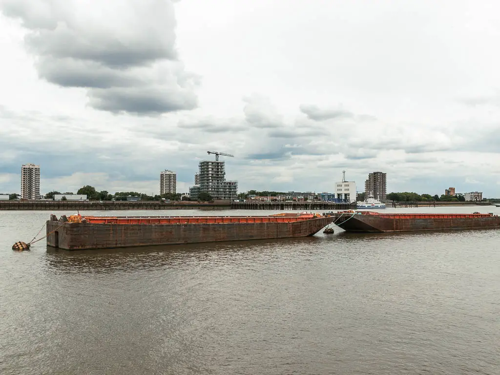 Two cargo boats sitting in the middle of the river near the end of the Tower Bridge Thames Barrier walk.