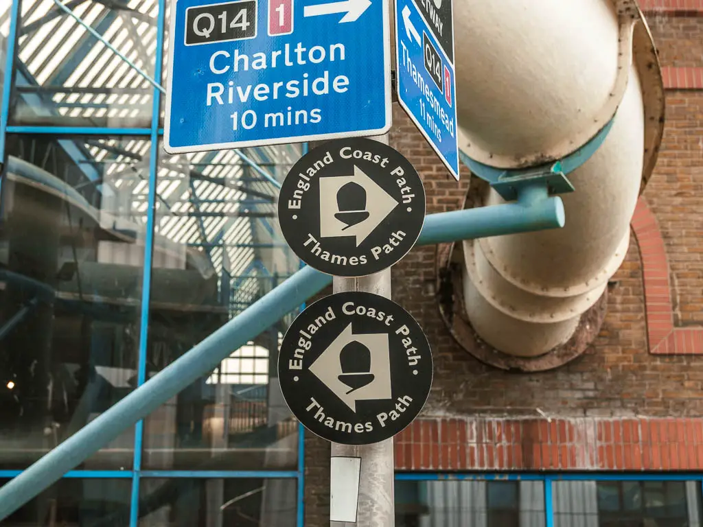 Two Thames Path and England coast oath black disc signs on a pole, at the end of the Tower Bridge to Thames Barrier walk.