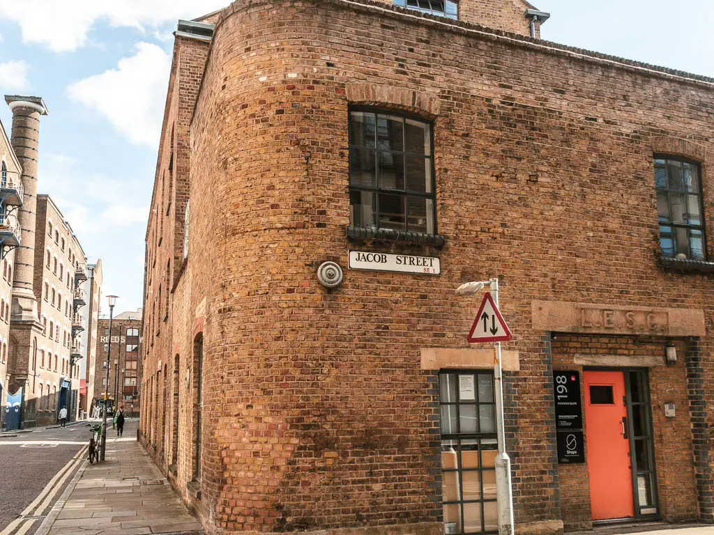 Looking at the corner of a brick houses, with a street sign saying 'Jacob Street'.