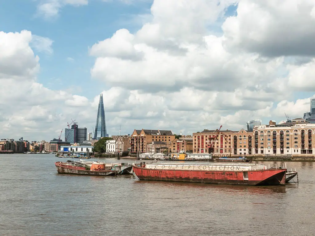 Looking across the river to a rusty cargo boat, row of apartments on the other side, and the shard in the distance. 