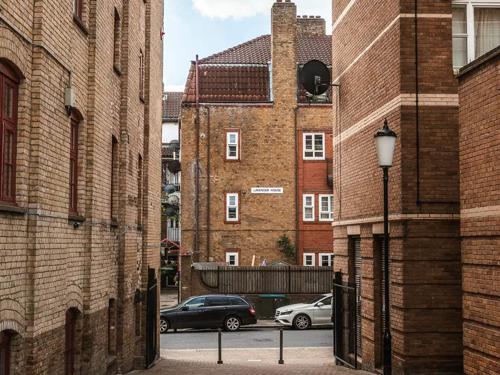 Looking along the path between the brick buildings to the road with parked cars.