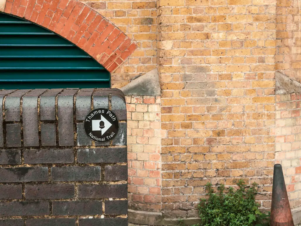 A thames path sign on the wall, with a white arrow pointing right, on the all between Tower Bridge and the Thames Barrier.