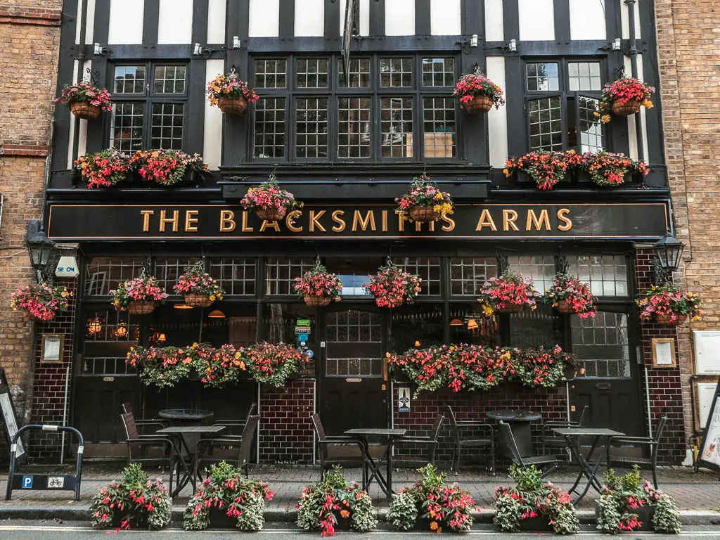 The facade of the Blacksmiths arms pub with lots of red flowers hanging outside.