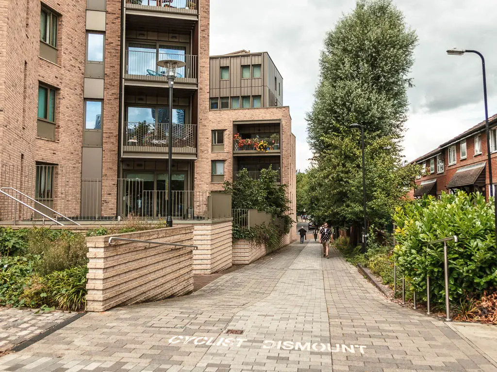 A walking path with apartments to the left and bushes to the right.