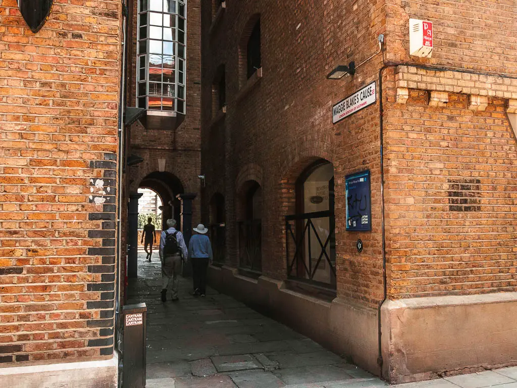 An ally between the brick buildings. There are some people walking along it.