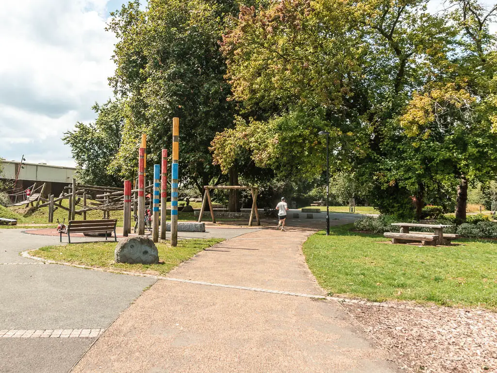 A path leading through the park with a playground to the left and trees ahead.