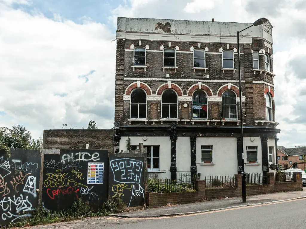 A three story brick building next to the road, with arch shaped windows and white peeling paint at the top.