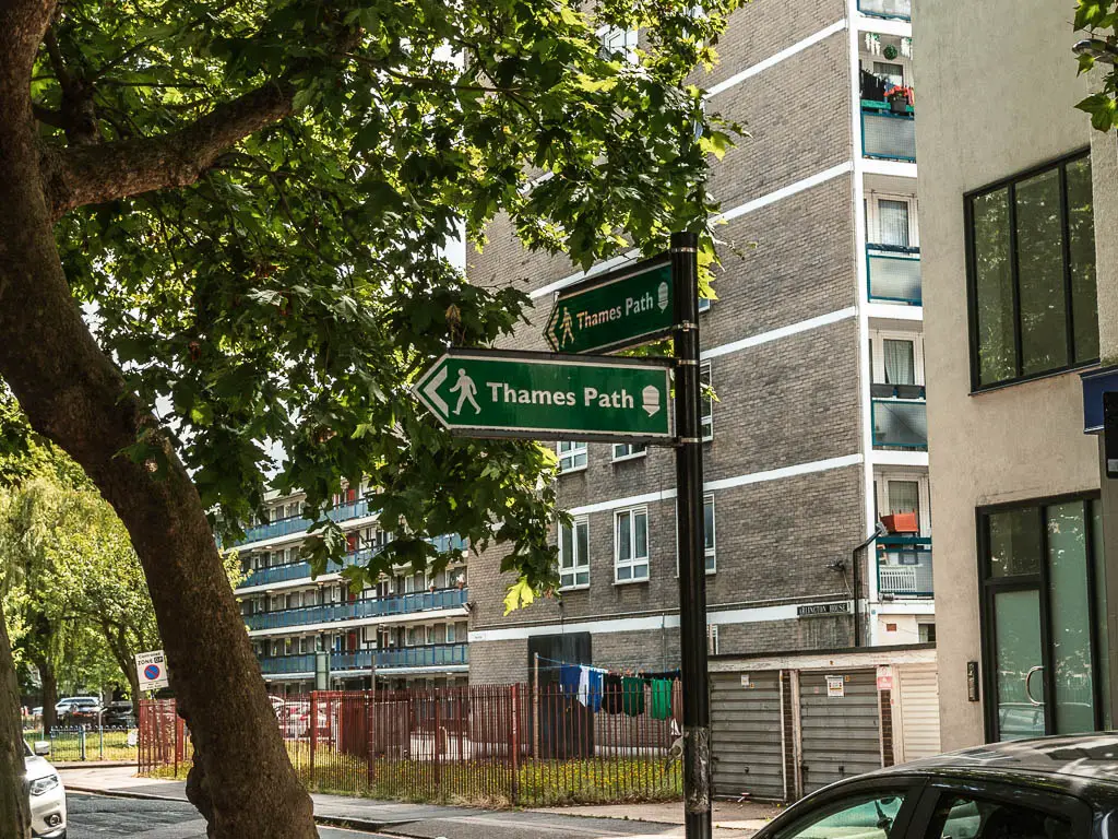 A green Thames path sign pointing left and back. 