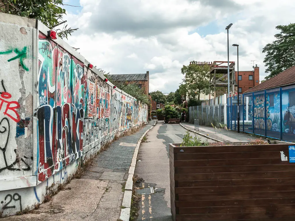 A road lined with a graffiti covered wall on the left.