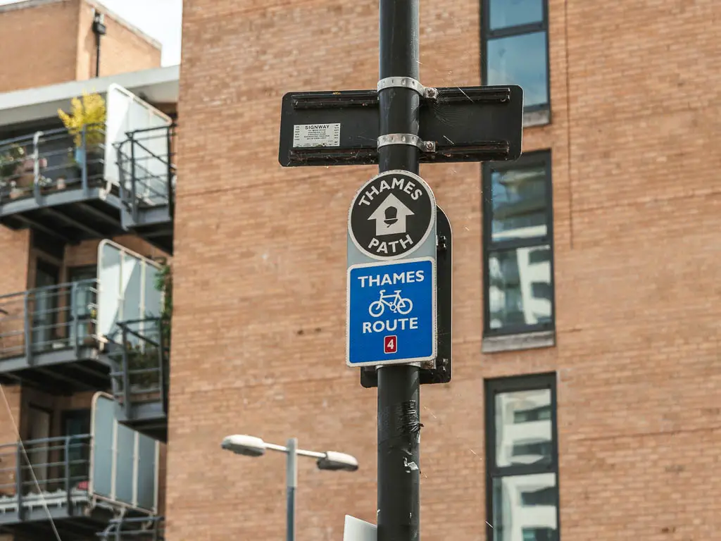 A black circle thames path sign on a black lamppost, with a white arrow pointing ahead.