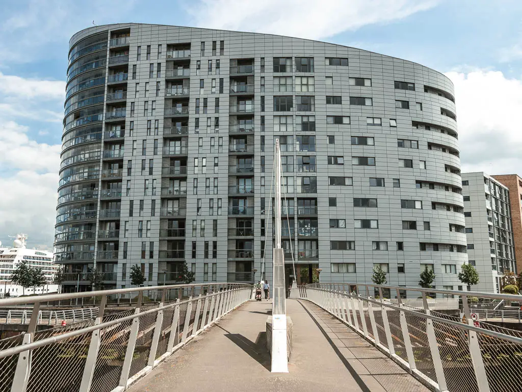 A bridge walking path leading towards a large grey apartment building.