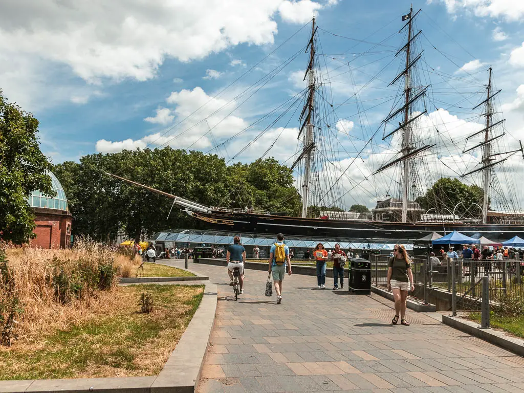 A wodę path leading to an old ship. There are lots of people walking along the path.