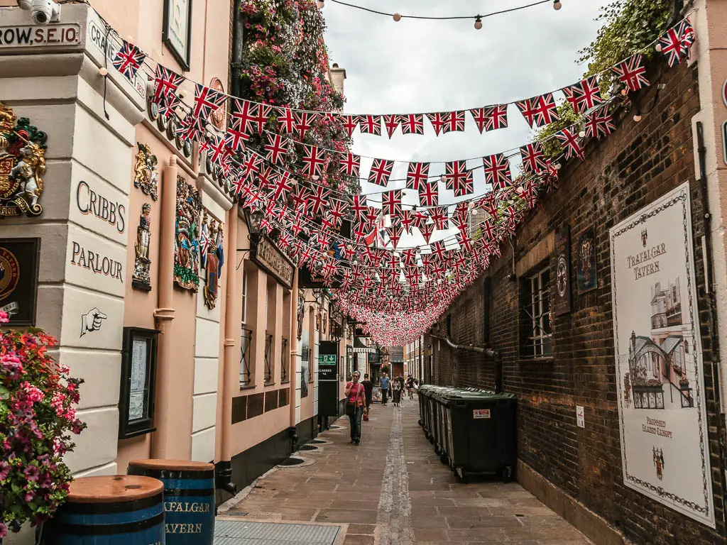 Looking along an alley way between a pub and brick wall, with Union Jack bunting hanging between them.