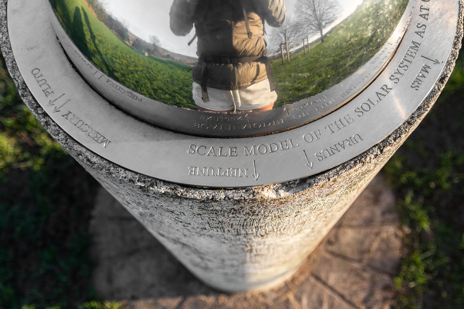 Looking down the edge of the sun model of the Otford Solar System, which is a reflective dome on top of a grey pillar. The planets are marked with arrows around the bottom edge of the dome. 