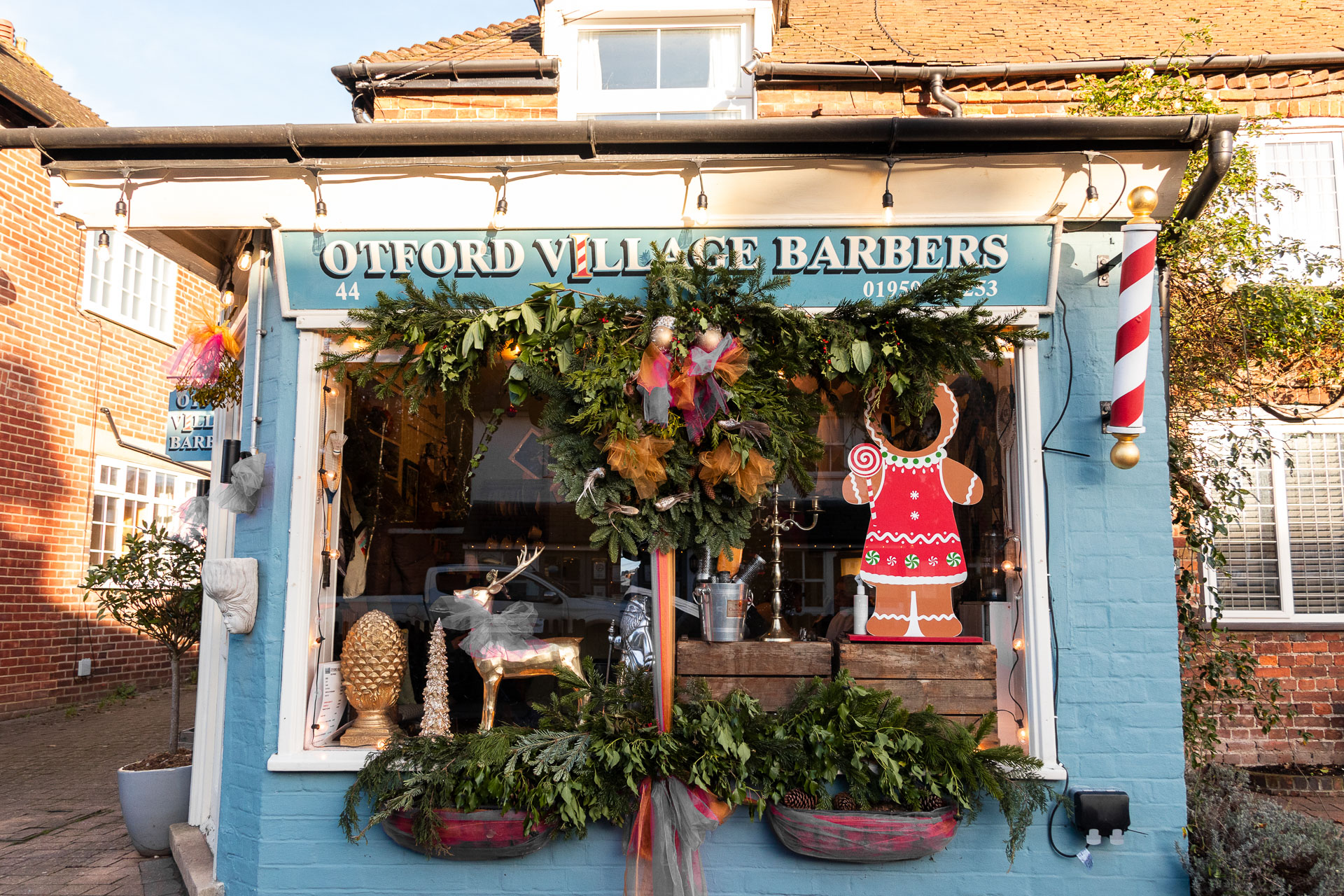 The otford village barbers, with a blue painted brick wall, and large window in the middle, decorated with Christmas stuff.