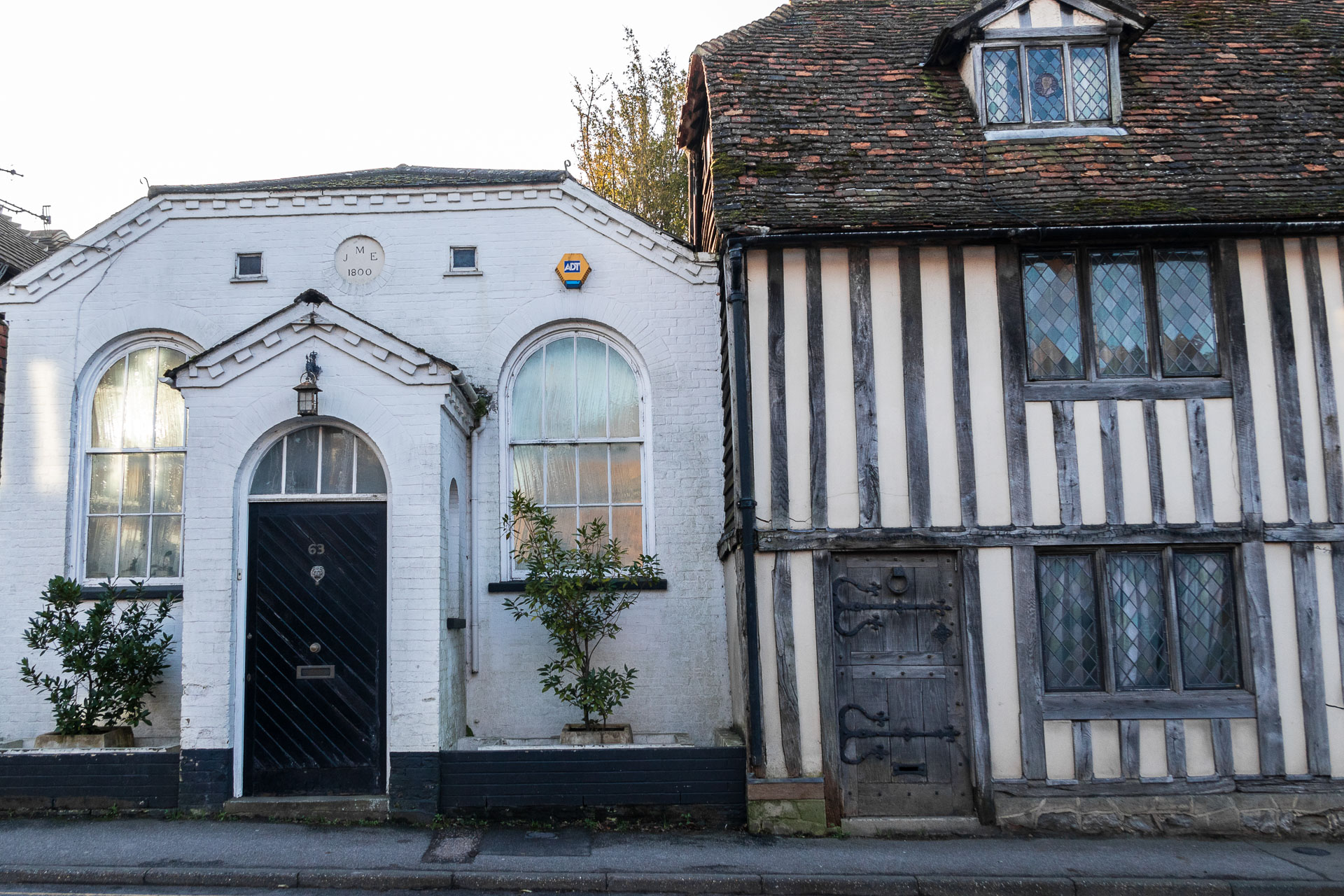 The facade of an elizabethan building on the right and white painted building with black door to the left in Otford. 