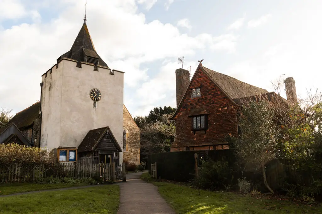 A path leading towards a church in Otford, with a cream facade and clock on the middle.