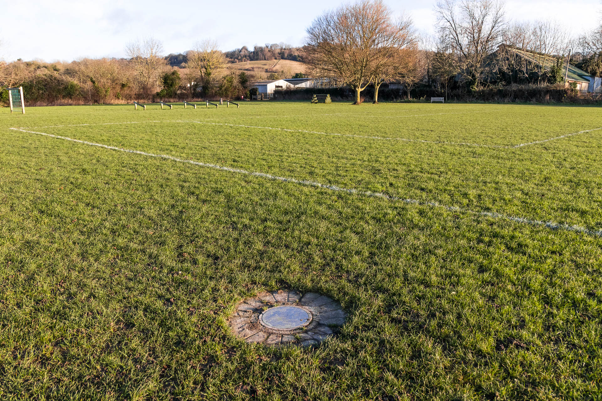 A flat grey marker for mars in the middle of a green grass sports field.