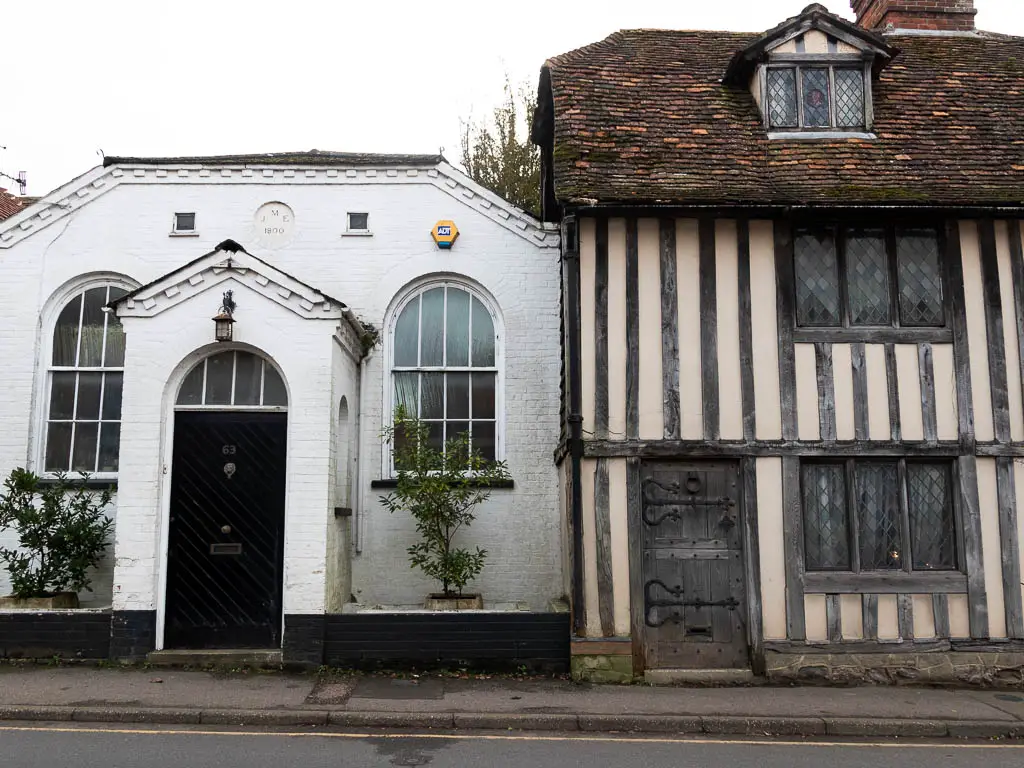 The facade of an Elizabethan cottage on the right and a white walled cottage on the left with a black door.