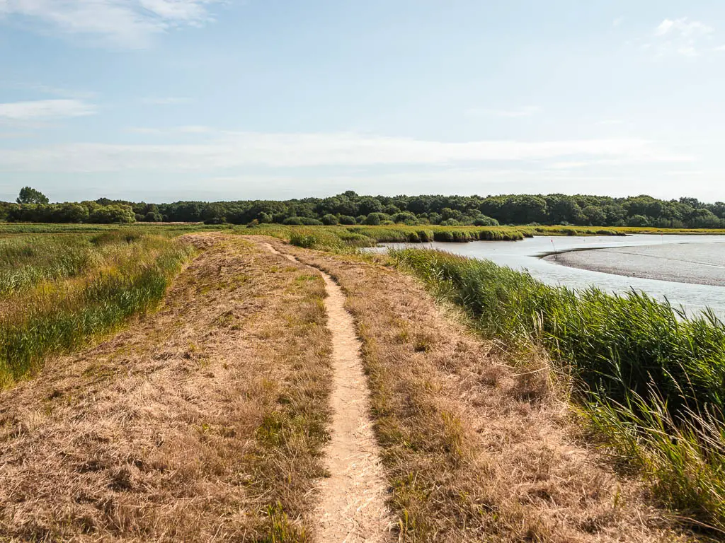 A narrow trail along a ridge, surround by meadows, with a river to the right.