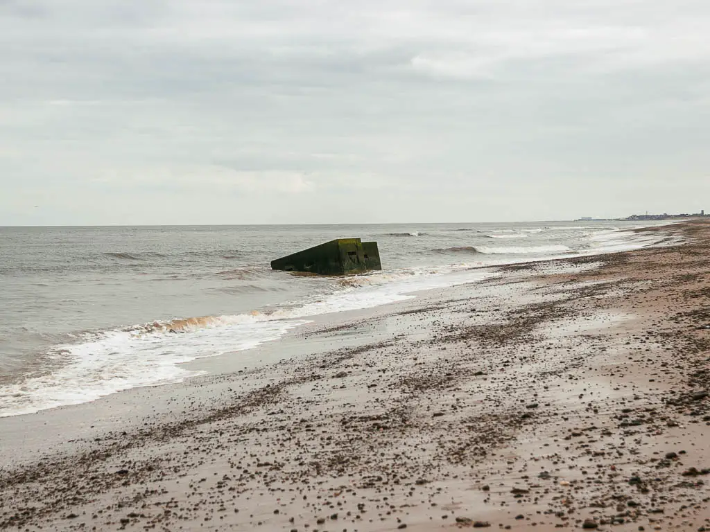 The rough sea where is meets the wet sand beach, with a war pillbox partially under the sea, on the walk from Dunwich to Kessingland.