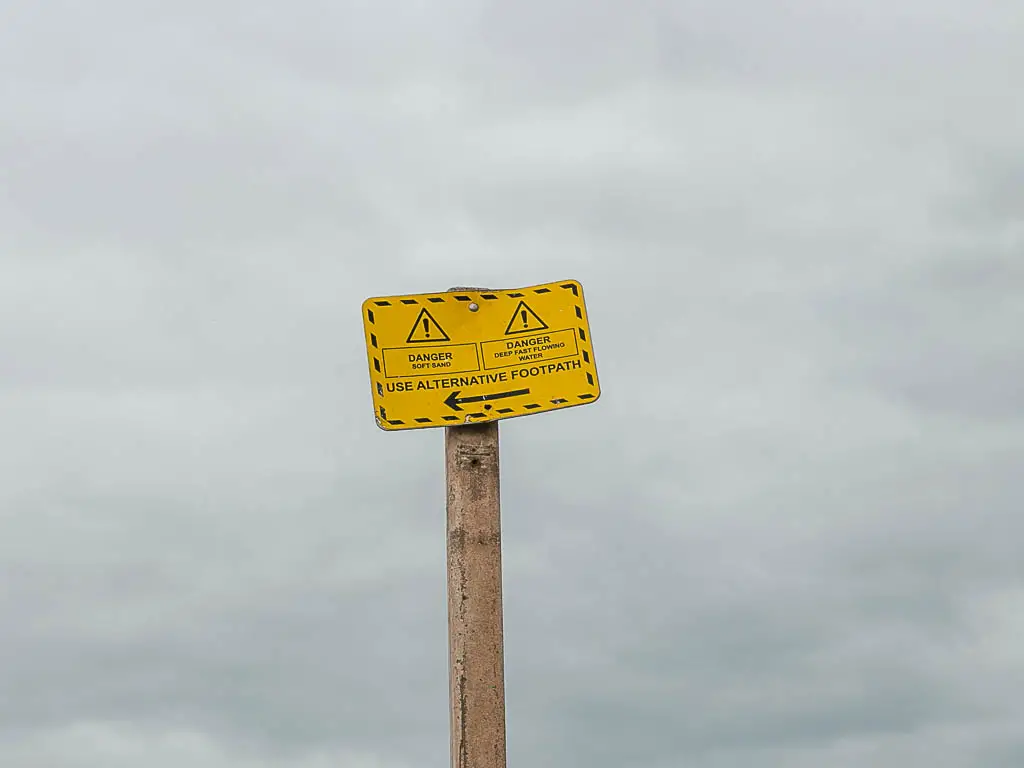 A yellow danger sign on a wooden post with a cloudy sky backdrop.