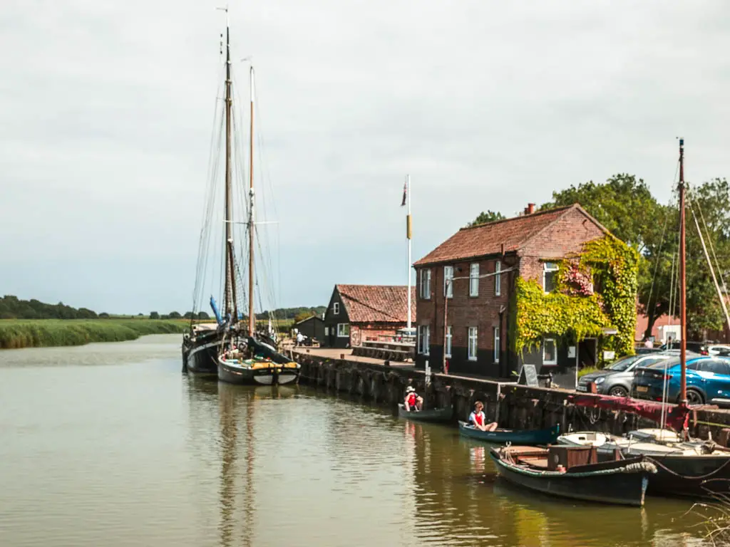 Looking along the river, with sailboats moored to the right side, and a house with ivy covering one of the walls.