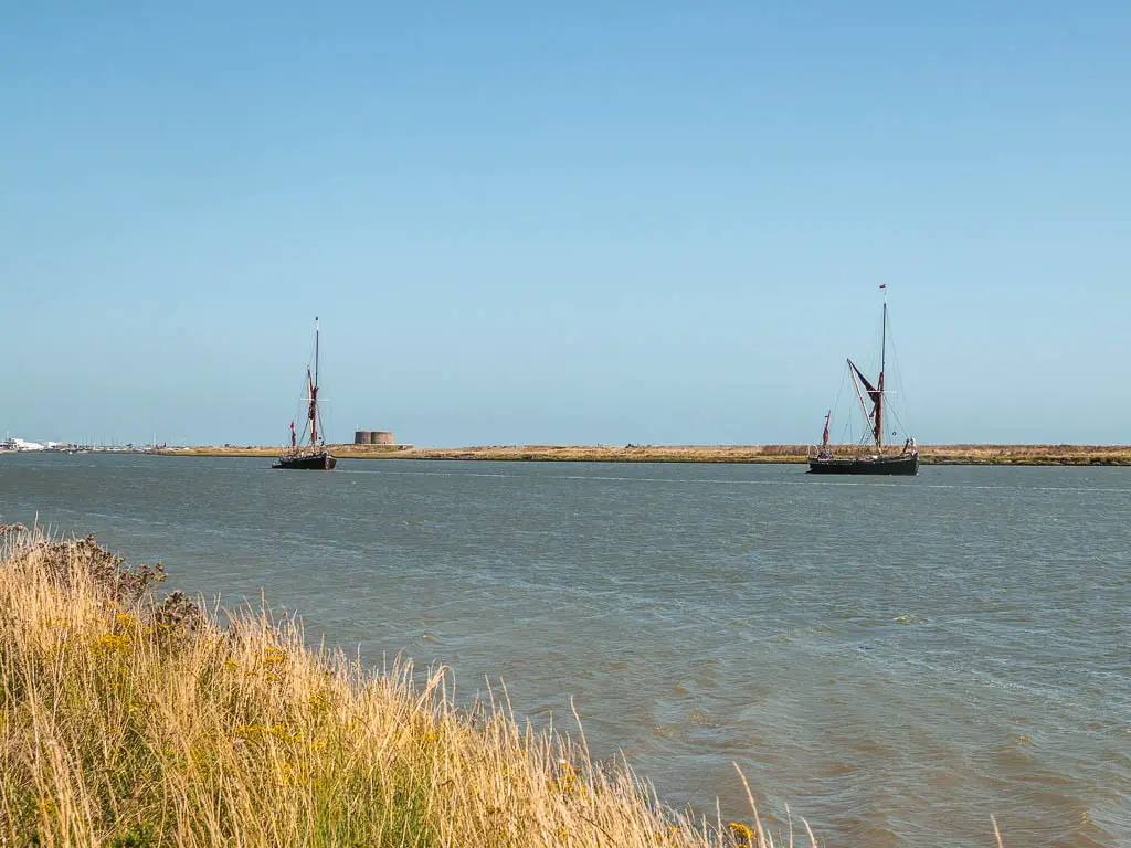 Two sailboats with their sails down, on the river.