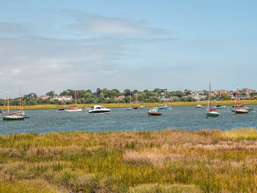 Looking across the grass bank to the river filled with various boats, on the walk from Orford to Snape.