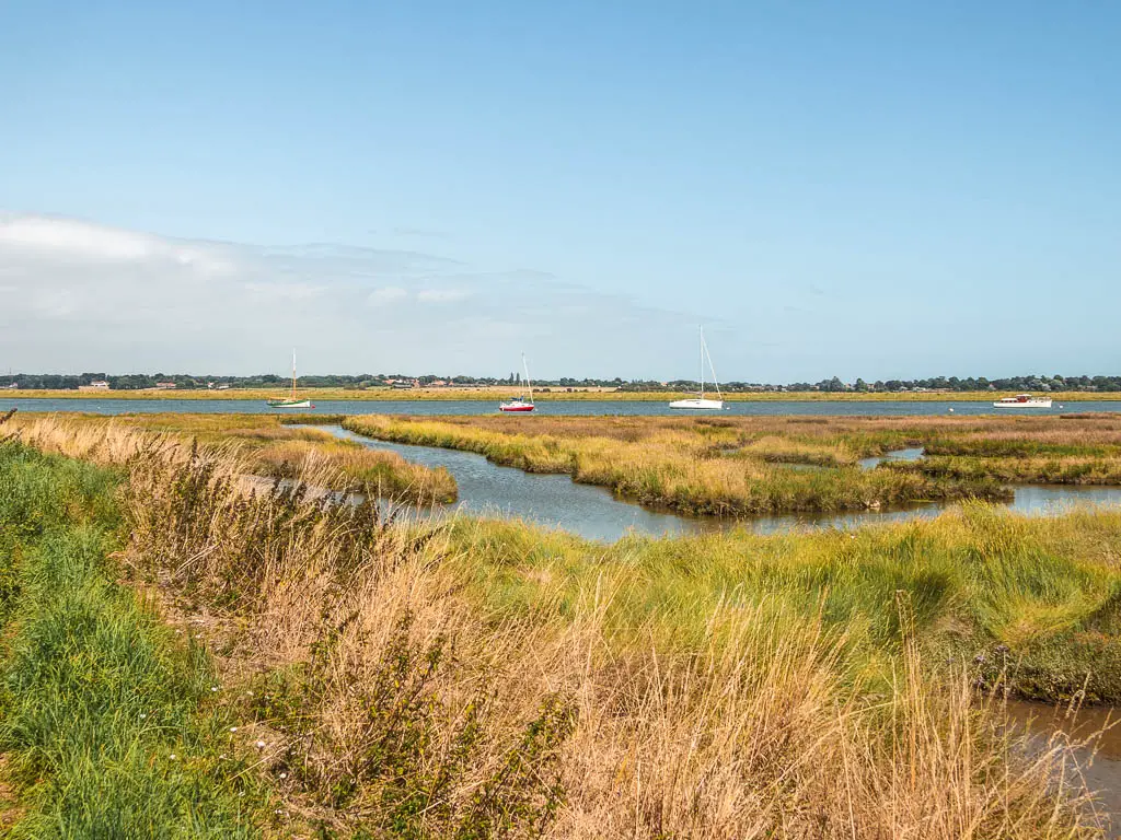 Looking across the grass marshland to the river, with a few sailboats dotted about, on the walk from Orford to Snape.