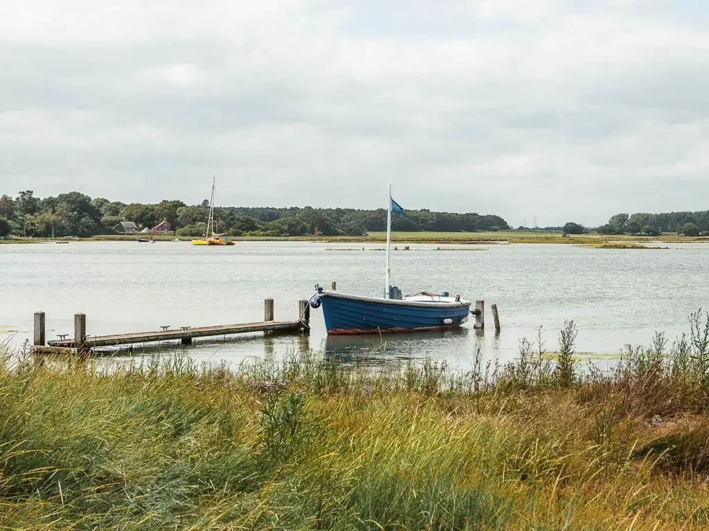 A small blue row boat sitting on the river, next to a wooden walkway, on the walk between Orford and Snape.